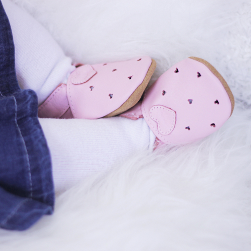 Tiny baby girl wearing pink soft leather baby shoes from Dotty Fish with cut-out heart design