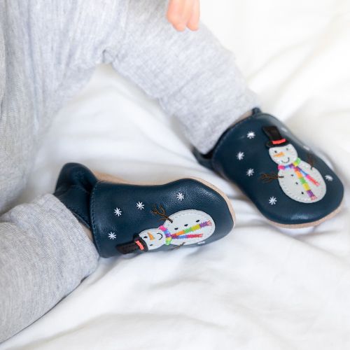 Toddler wearing navy leather Dotty Fish first walker shoes with white snowman wearing black hat and embroidered rainbow scarf design.