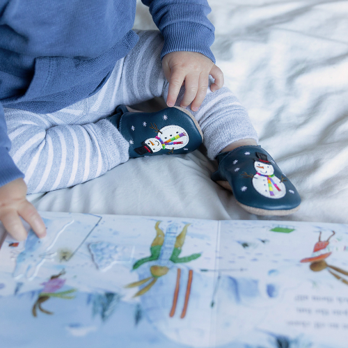 Baby wearing Jolly Snowman soft leather baby shoes while reading a book 