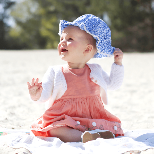 Baby girl wearing Dotty fish white flower sandals while sitting at the beach.
