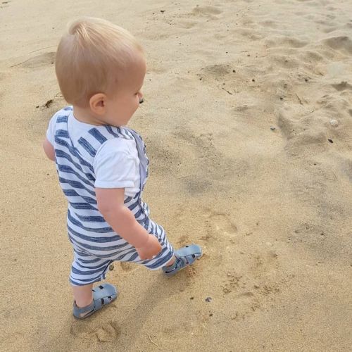 Toddler walking on the beach wearing grey soft sole sandals from Dotty Fish 
