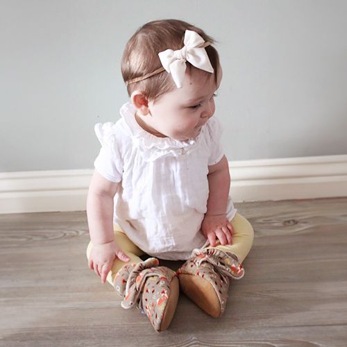 Baby girl sitting wearing light brown cotton Dotty Fish booties with white fleece lining and woodland animal pattern.
