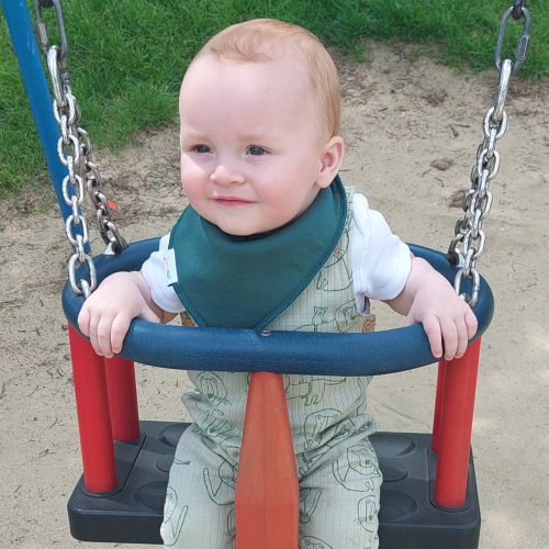 Baby wearing forest green baby bib while playing outside