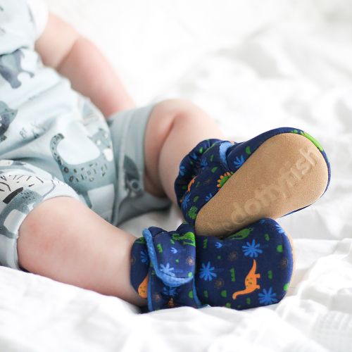 Dinosaur themed baby booties with adjustable fastening worn by young baby boy