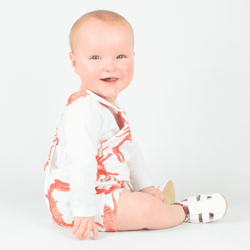 White leather baby sandals with non-slip suede soles being worn by little baby while sitting 