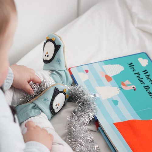 Baby boy sitting, wearing mint green Dotty Fish shoes with white and black penguin design, looking at a book.