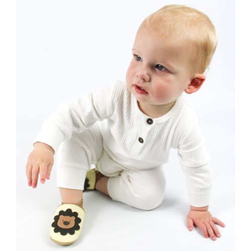 Baby wearing cream Dotty Fish shoes with lion design and white baby grow, sitting on floor.