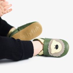 Baby boy sitting on floor wearing green Dotty Fish shoes with cream bear design.