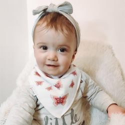 Baby girl wearing Dotty Fish white cotton bandana bib with pink butterfly pattern.