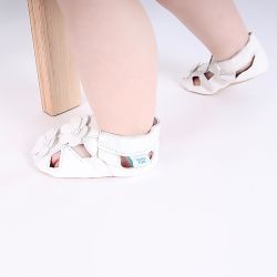 Baby girl standing, wearing white Dotty Fish barefoot sandals, with white flowers.