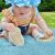 Toddler girl sitting on blanket wearing white leather Dotty Fish first walker barefoot sandals with white flowers.