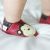 Toddler wearing red Dotty Fish shoes with brown and cream monkey design.