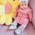 Girl wearing blue rainbow booties, sitting with yellow flower cushion.
