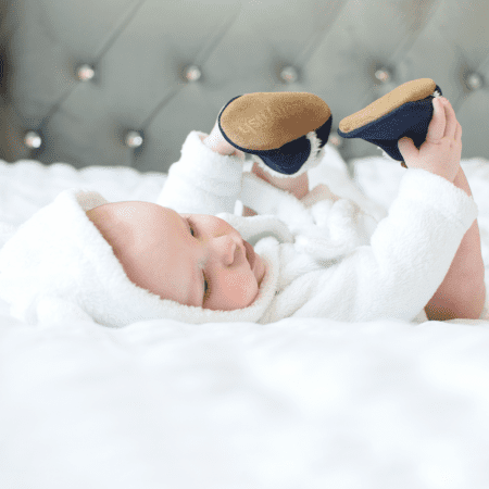 Baby on bed wearing navy suede slippers from Dotty Fish.