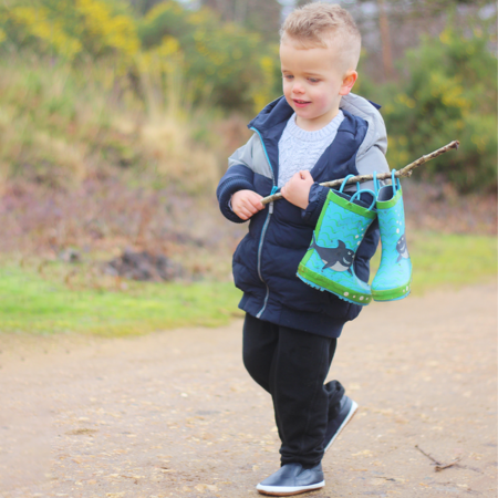 Little boy wearing Dotty Fish shoes carrying his wellies