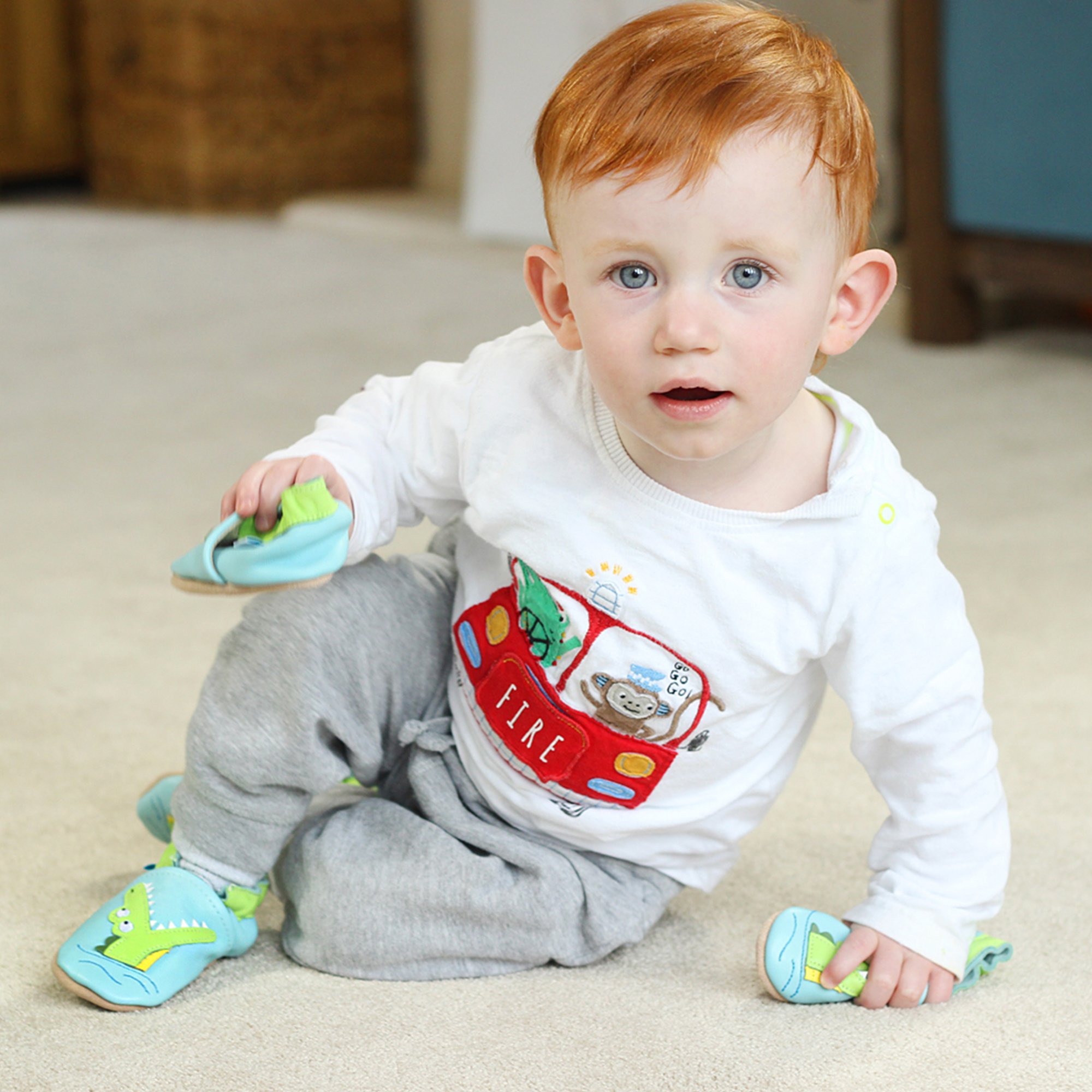 Toddler boy wearing blue baby leather shoes with green crocodile design.