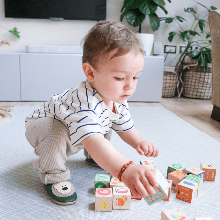 Toddler boy playing with toys, wearing leather shoes with bear design.