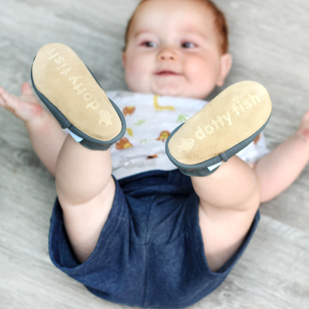 Baby boy lying down with feet in the air and wearing Dotty Fish shoes.