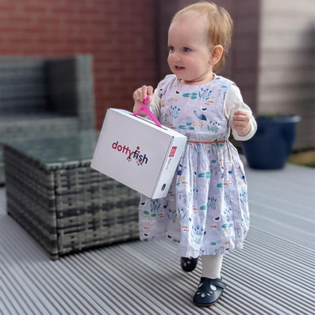 Toddler wearing navy rubber sole shoes, carrying Dotty Fish shoe box.